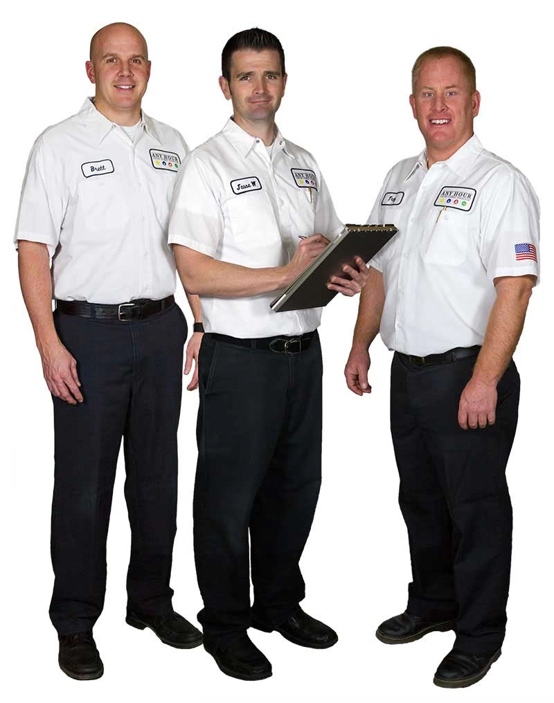 Three men in white uniforms, labeled with name tags, stand together smiling. The middle man holds a clipboard, suggesting a professional setting.