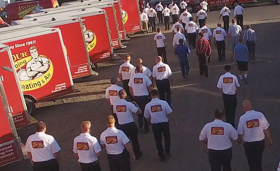 A group of people in uniform shirts with a logo walk towards red service trucks labeled Heating & Air in a parking lot, conveying teamwork and purpose.