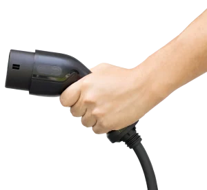 A hand tightly grips a black electric vehicle charging plug, set against a plain background. The image conveys readiness and focus on sustainability.