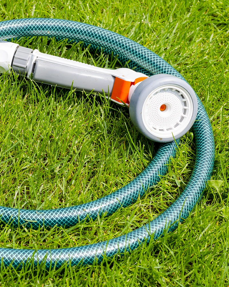 A coiled garden hose with a gray spray nozzle rests on vibrant green grass. The scene conveys a feeling of freshness and outdoor activity.