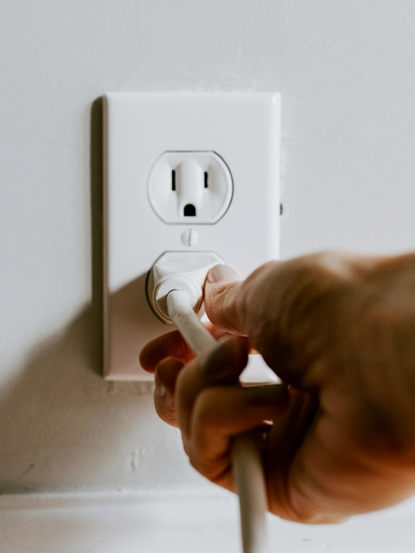 A hand is seen plugging a white cord into a wall electrical outlet. The scene conveys a sense of action, focusing on connectivity and power.