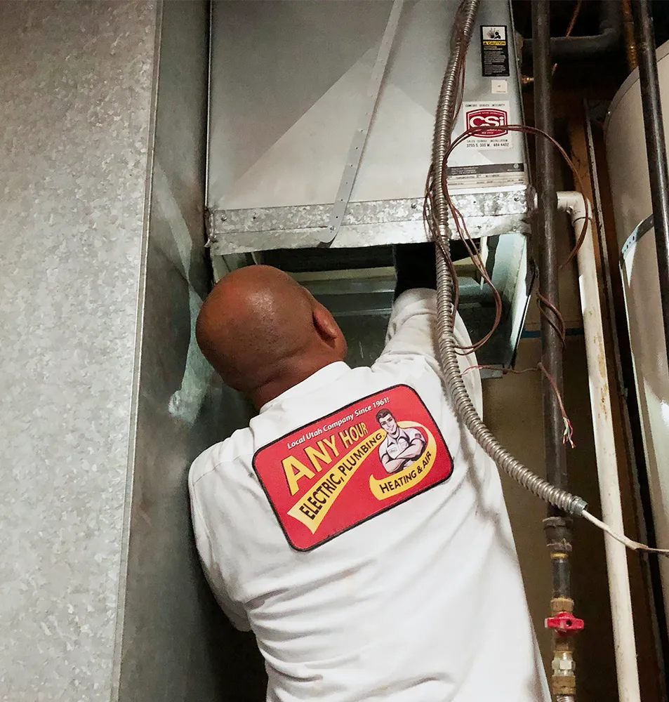 A technician in a white uniform with a logo inspects an HVAC unit in a confined space. The setting conveys a focused and professional atmosphere.