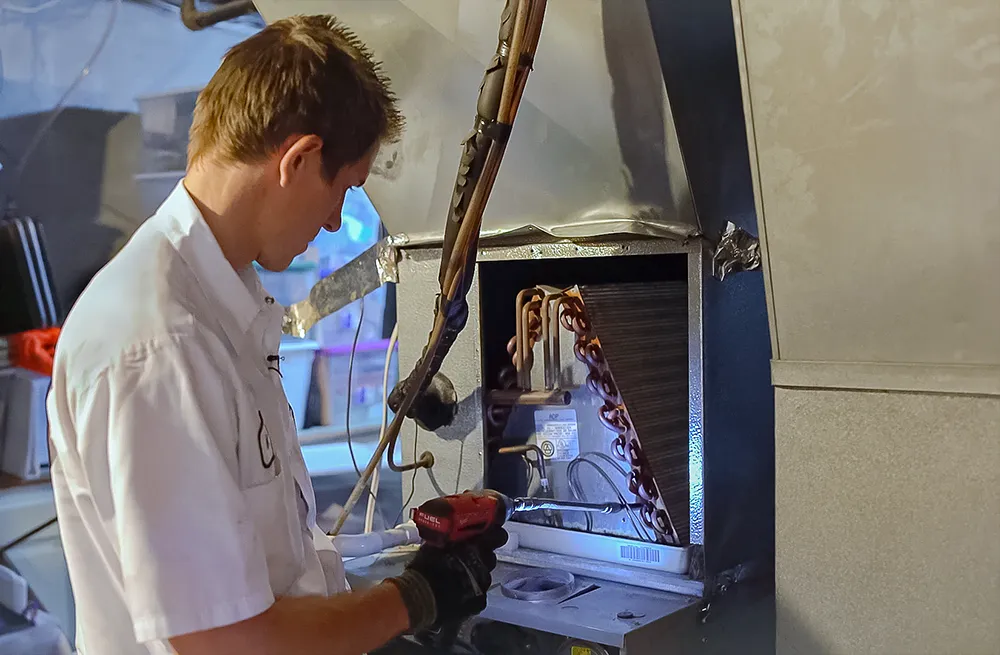 Technician in a white shirt repairs an HVAC unit, using a red tool. The scene suggests a focused, diligent atmosphere, highlighting maintenance work.