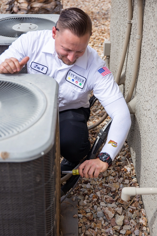 Technician in a white uniform adjusts outdoor AC unit. Focused expression, surrounded by rocky ground, conveying professionalism and attention to detail.